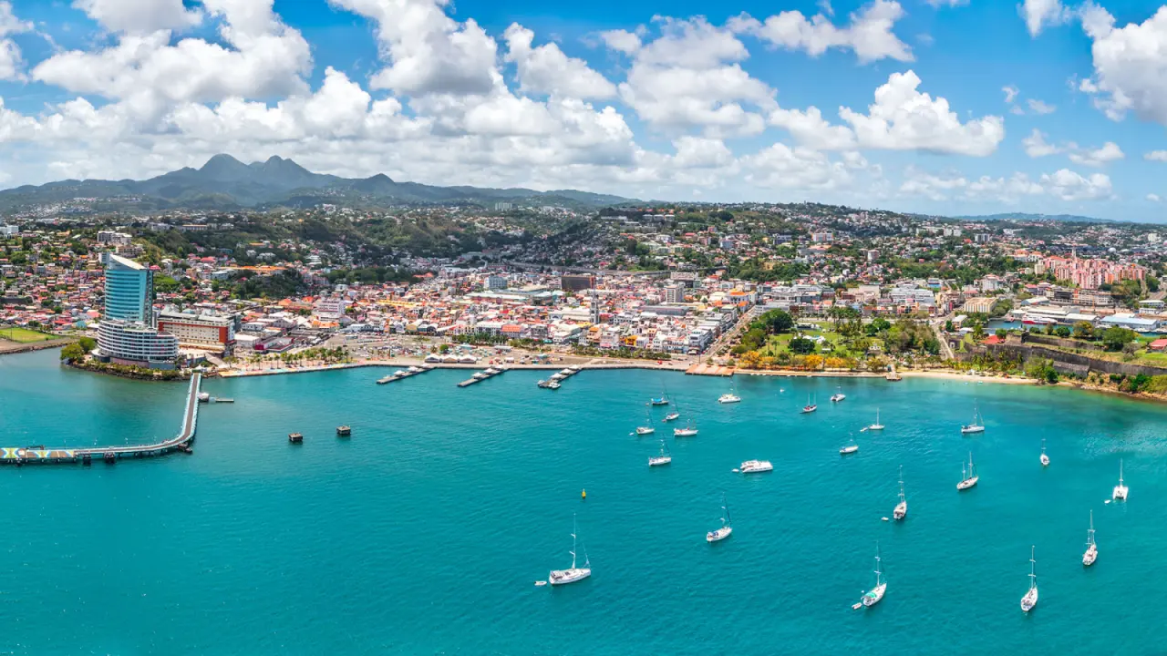 Vue aérienne de la baie de Fort-de-France en Martinique : mer turquoise parsemée de voiliers et tour Lumina en bord de mer.