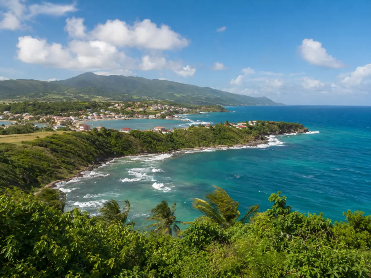 Littoral sauvage de La Trinité en Martinique : baie d'eau turquoise, vagues blanches et collines verdoyantes au loin.