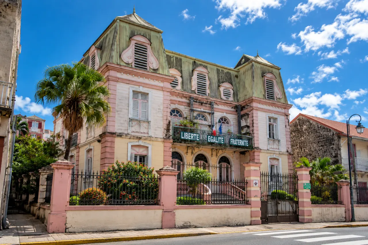 Ancienne mairie de Martinique à façade rose et blanche, architecture coloniale, persiennes et balcon orné de la devise Liberté Égalité Fraternité.