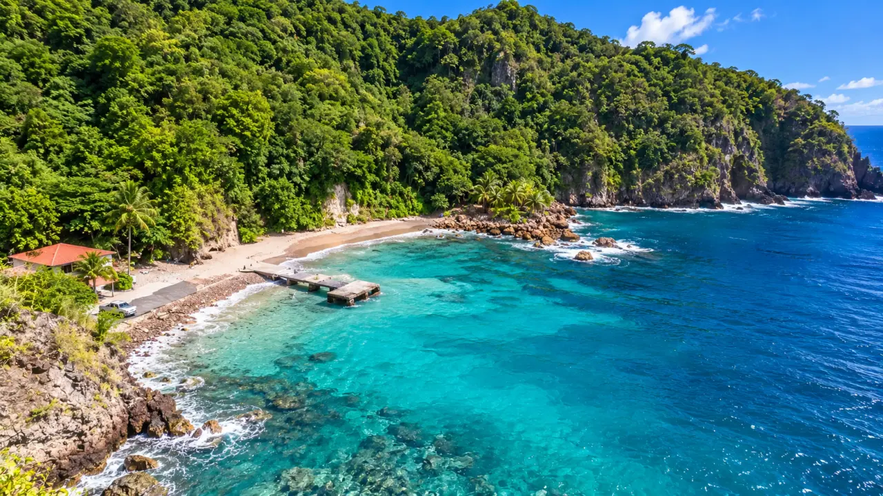 Anse tropicale de Guadeloupe bordée de falaises volcaniques et de forêt luxuriante, avec eaux turquoise et plage de sable.