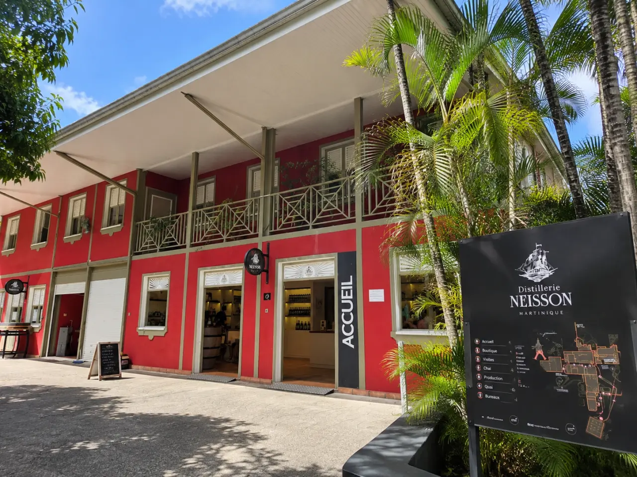 Distillerie Neisson en Martinique, bâtiment traditionnel rouge avec galerie, boutique d’accueil et végétation tropicale.