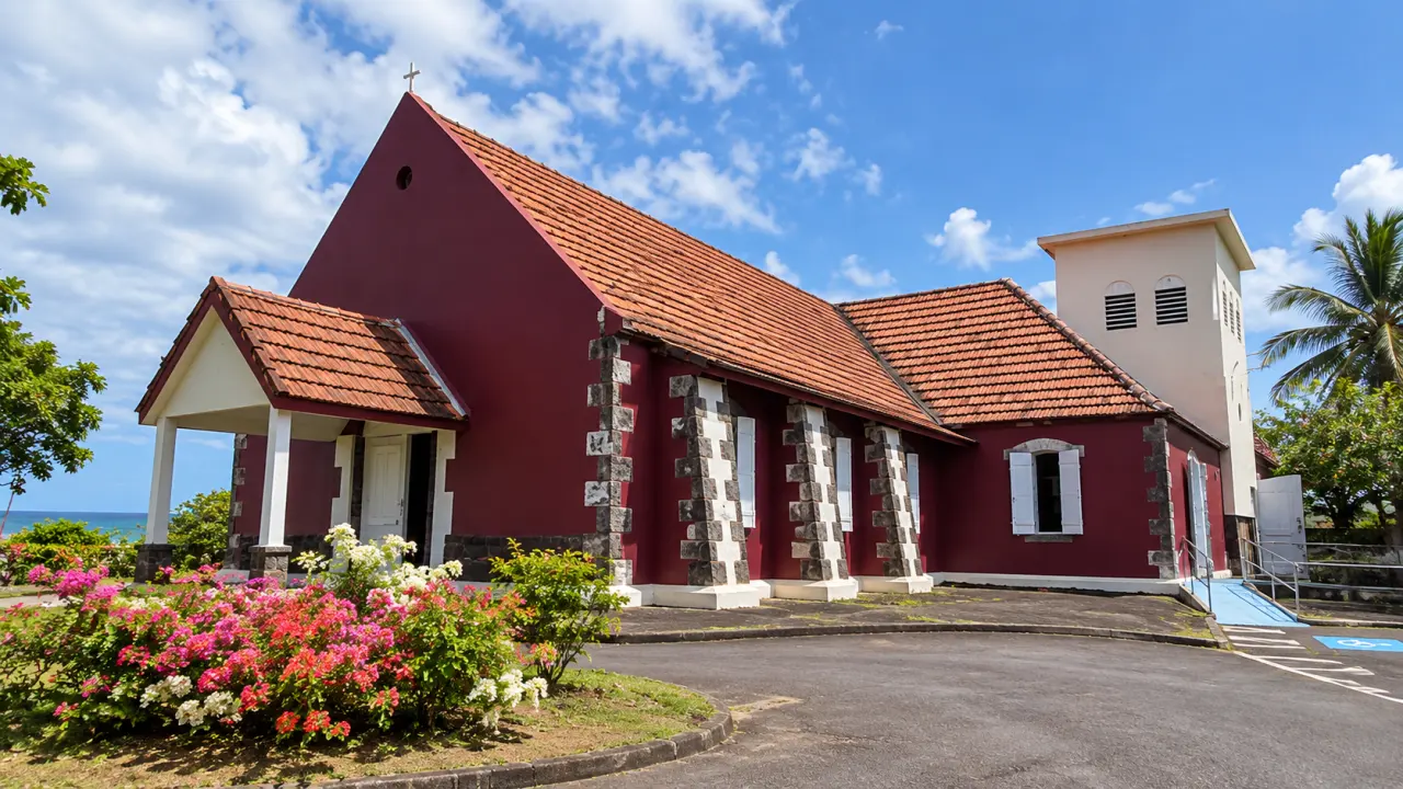 Église de Martinique à l’architecture créole, façade rouge bordeaux, toiture en tuiles et clocher blanc au cœur d’un paysage tropical.