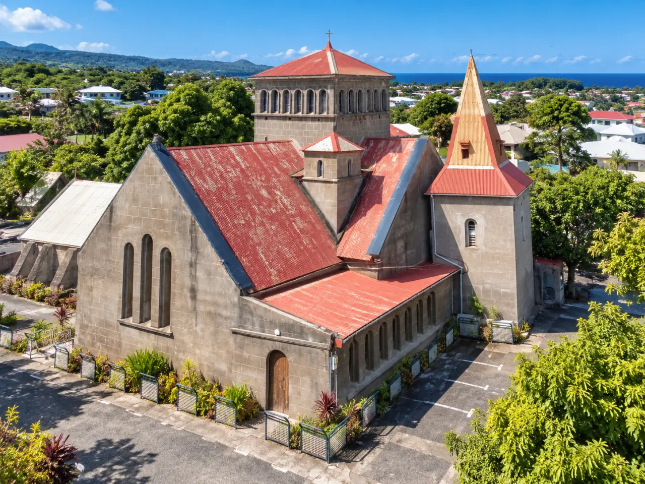 Église en Guadeloupe avec architecture en pierre et toitures rouges, vue aérienne sous un ciel bleu.