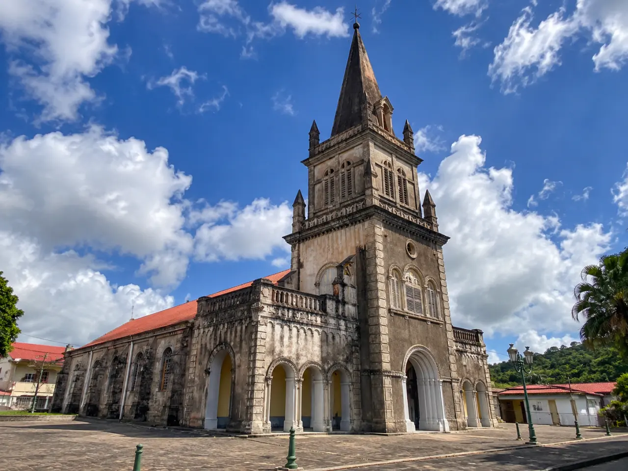 Église historique de Martinique, avec sa façade en pierre, ses arcades, son clocher monumental et son clocher à flèche sous un ciel bleu nuageux.