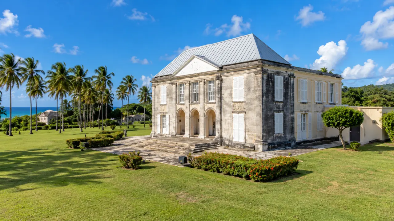 Habitation historique de Guadeloupe entourée de jardins tropicaux et de cocotiers, avec architecture coloniale et vue sur la mer.