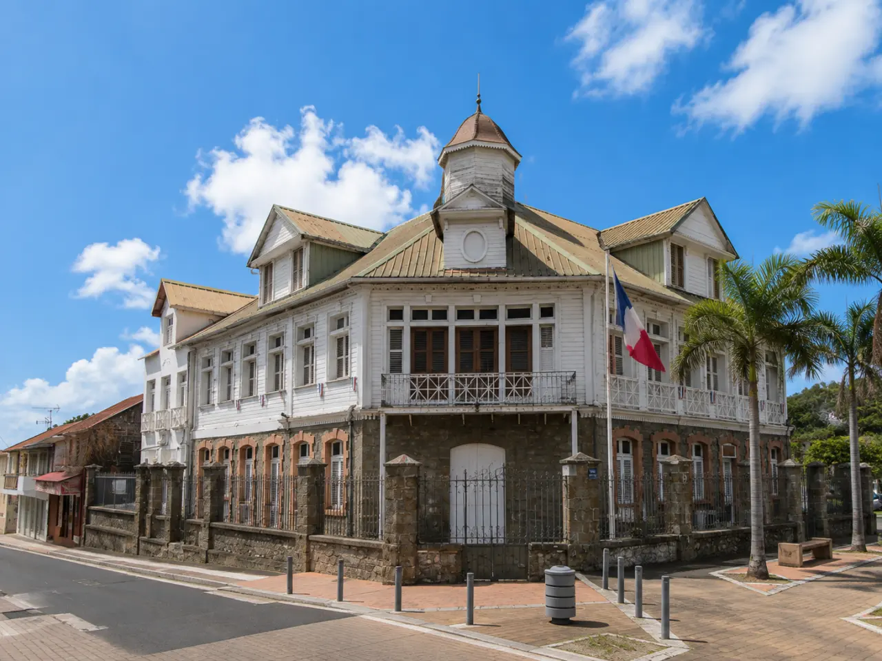 Façade en pierre et bois de l'hôtel de ville du François en Martinique avec le drapeau français sous le soleil.