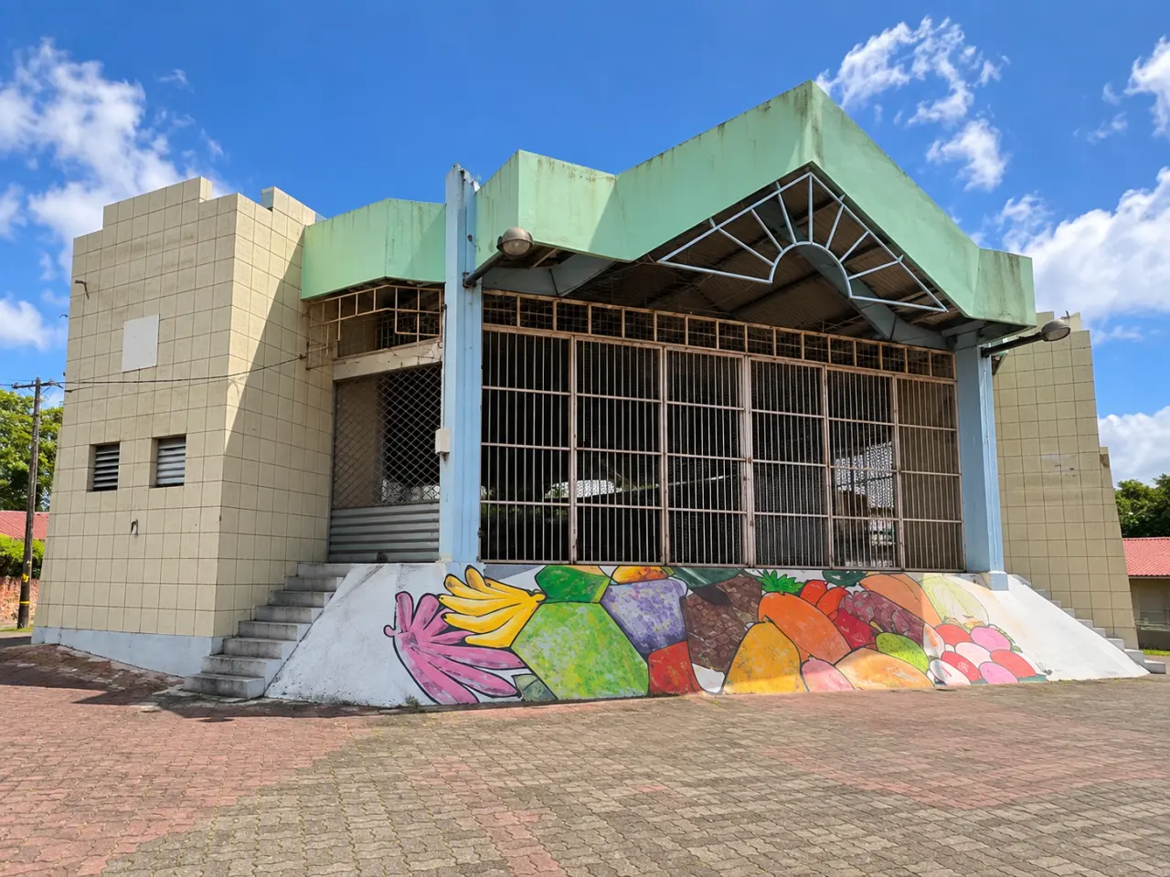 Marché couvert en Martinique avec façade carrelée, structure vert pastel, grilles métalliques et fresque colorée représentant des fruits tropicaux.