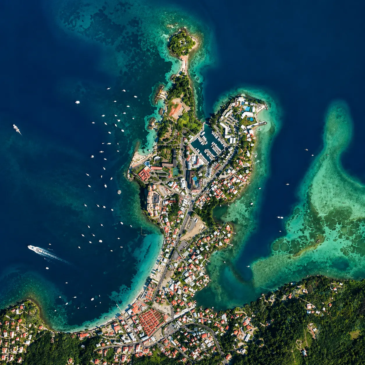 Vue aérienne verticale de la Pointe du Bout : presqu'île boisée s'avançant dans une mer bleu foncé et lagon turquoise.