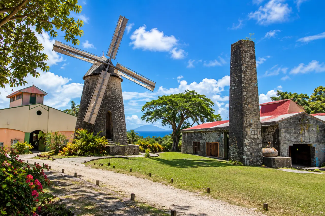 Moulin à vent de Guadeloupe et ancienne habitation sucrière avec cheminée en pierre sous un ciel bleu.