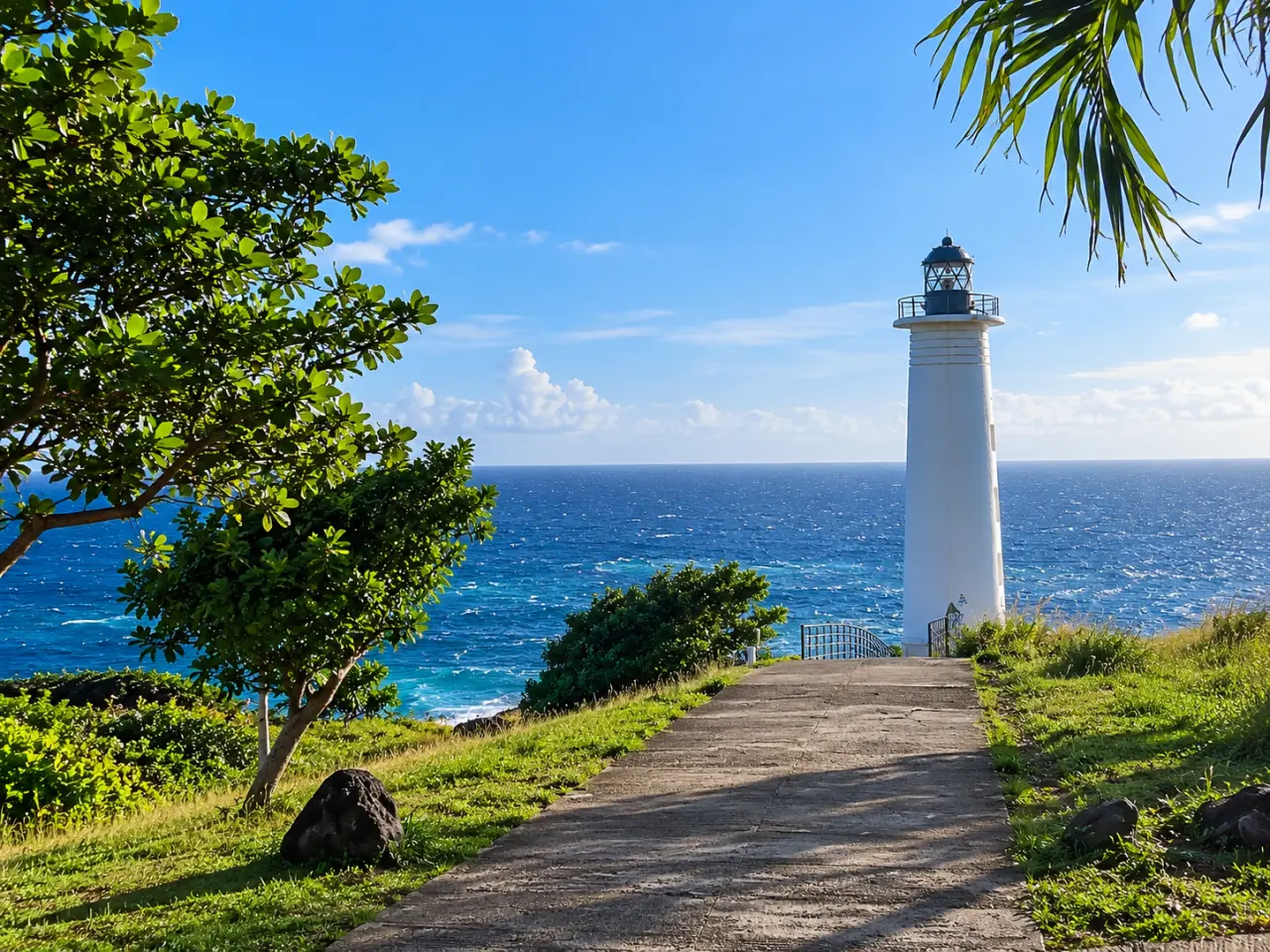 Phare de Guadeloupe au bord de l’océan, vue sur un phare blanc depuis un sentier côtier sous un ciel bleu.