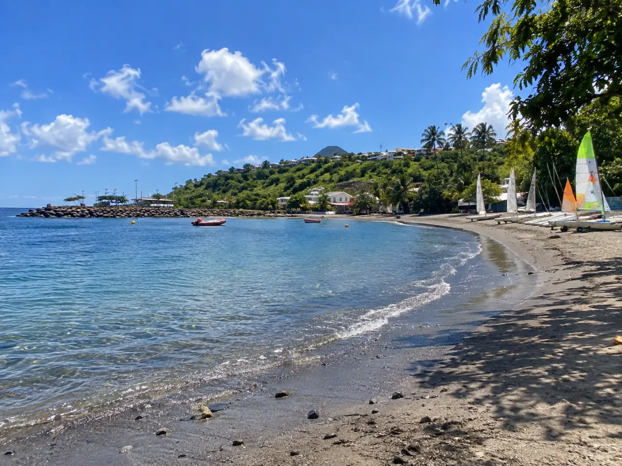 Plage de l’Anse Madame à Schœlcher en Martinique, avec ses eaux calmes, ses voiliers, sa plage et les collines verdoyantes en arrière-plan.