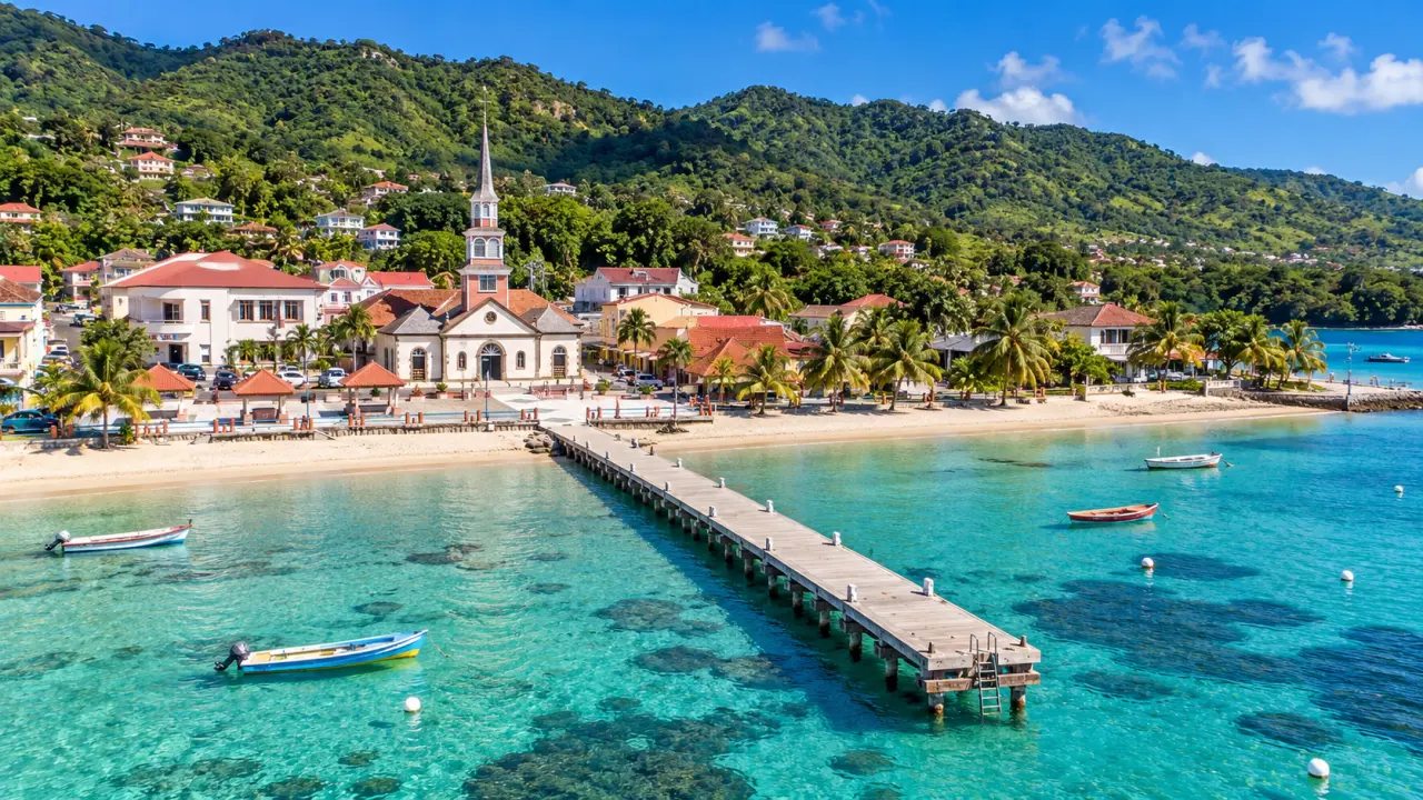 Plage des Anses d'Arlets en Martinique avec ponton, église, maisons créoles, cocotiers et eaux turquoise de la baie.