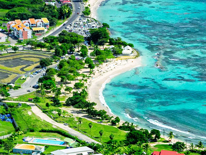 Vue aérienne de la plage des Raisins Clairs à Saint-François : sable blanc en croissant, lagon turquoise et arbres l'ombrant.