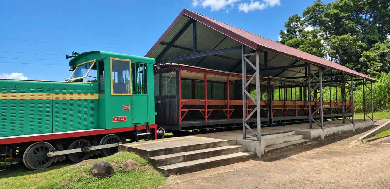Train touristique de Sainte-Marie en Martinique, locomotive verte « Moïse » et wagons ouverts sous une grande structure couverte au cœur d’un paysage tropical.