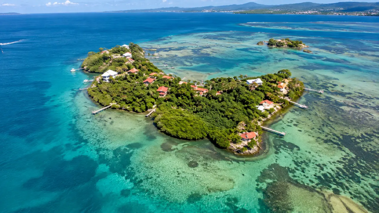 Vue aérienne d'un îlet de martinique entouré de récifs coralliens et d'eaux turquoise, avec habitations et pontons.