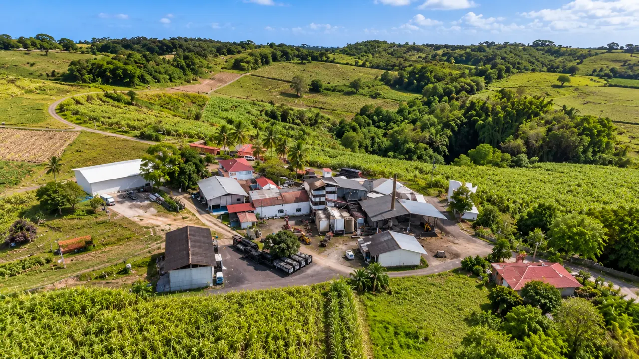 Vue aérienne d'une exploitation agricole en Guadeloupe entourée de champs verdoyants, de bâtiments agricoles et de collines tropicales.