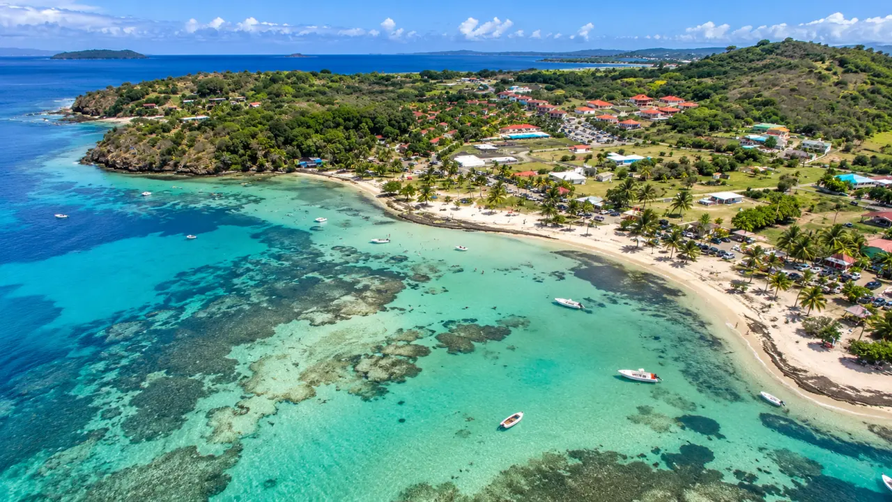 Vue aérienne de la plage du Robert en Martinique, avec eaux turquoise, récifs coralliens, cocotiers, bateaux et paysages verdoyants.