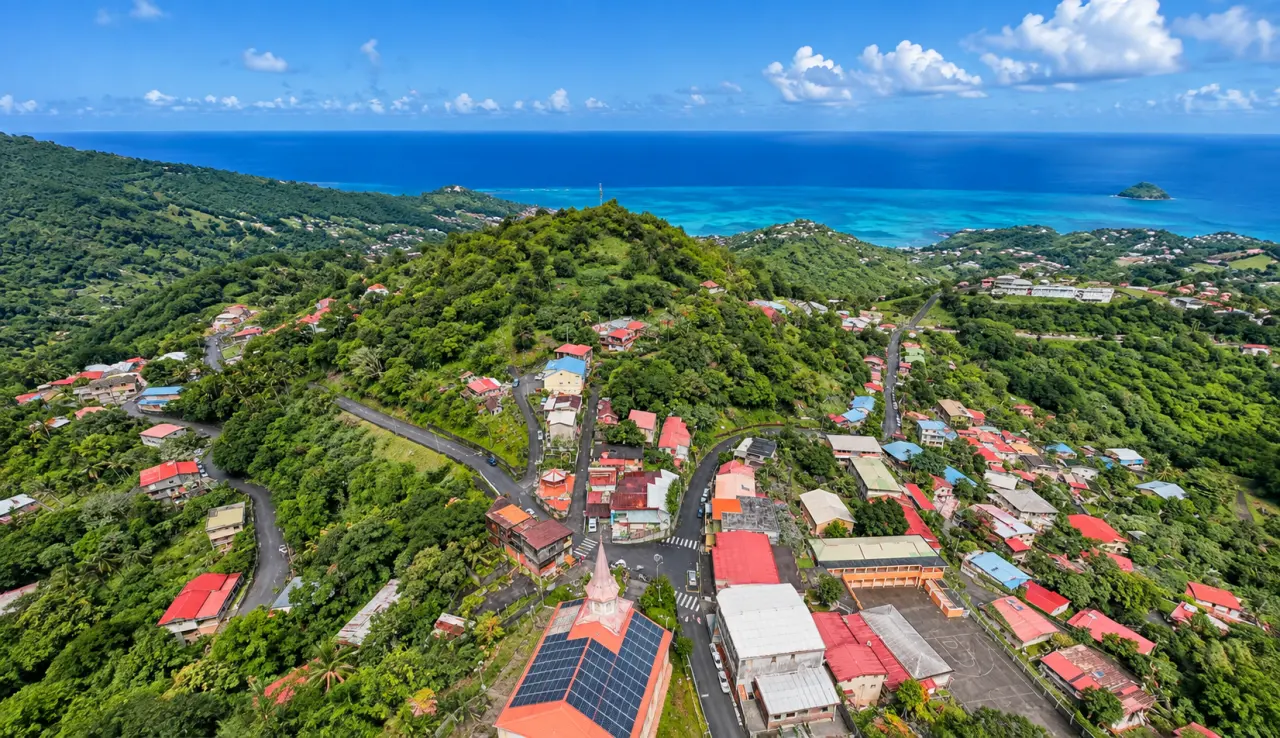 Vue aérienne du bourg du Morne-Vert en Martinique, entouré de végétation tropicale avec les collines verdoyantes et la mer turquoise en arrière-plan.