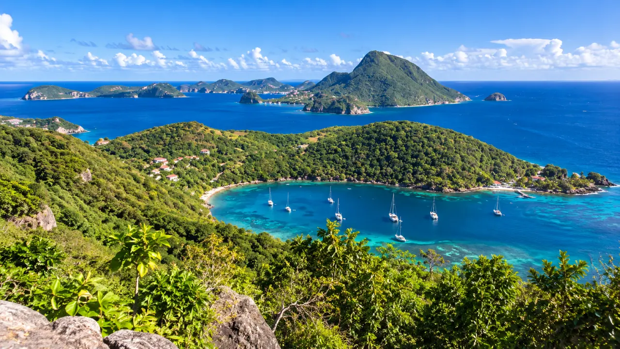 Vue panoramique sur les Saintes en Guadeloupe depuis les hauteurs, avec baie turquoise, végétation tropicale et îlets volcaniques.