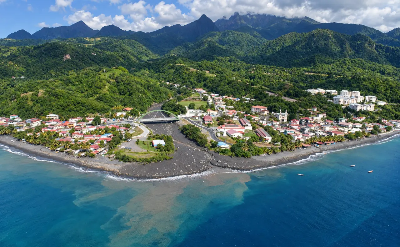 Le Prêcheur en Martinique vu du ciel, avec son bourg côtier, sa plage de sable noir, l’embouchure de la rivière et les montagnes verdoyantes en arrière-plan.