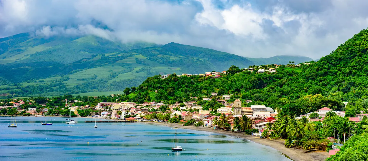 Ville côtière de Saint-Pierre en Martinique, installée au bord de l'eau au pied de montagnes verdoyantes sous les nuages. 