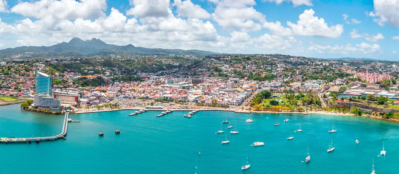 Vue aérienne de la baie de Fort-de-France en Martinique : mer turquoise parsemée de voiliers et tour Lumina en bord de mer. 