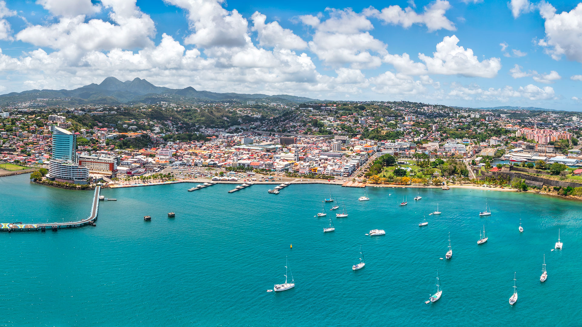 Vue aérienne de la baie de Fort-de-France en Martinique : mer turquoise parsemée de voiliers et tour Lumina en bord de mer.