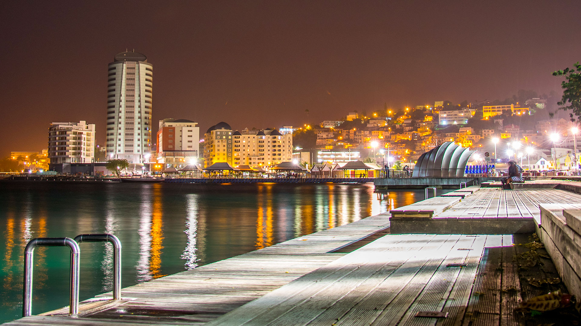 Vue nocturne du Malécon à Fort-de-France : promenade en bois éclairée au bord de l'eau face aux lumières de la ville.