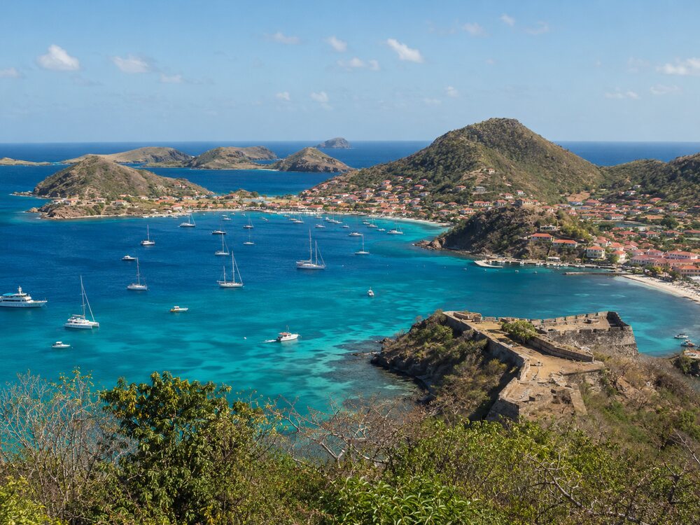 Baie des saintes avec ses bateaux amarrés et ses collines sous un ciel ensoleillée.