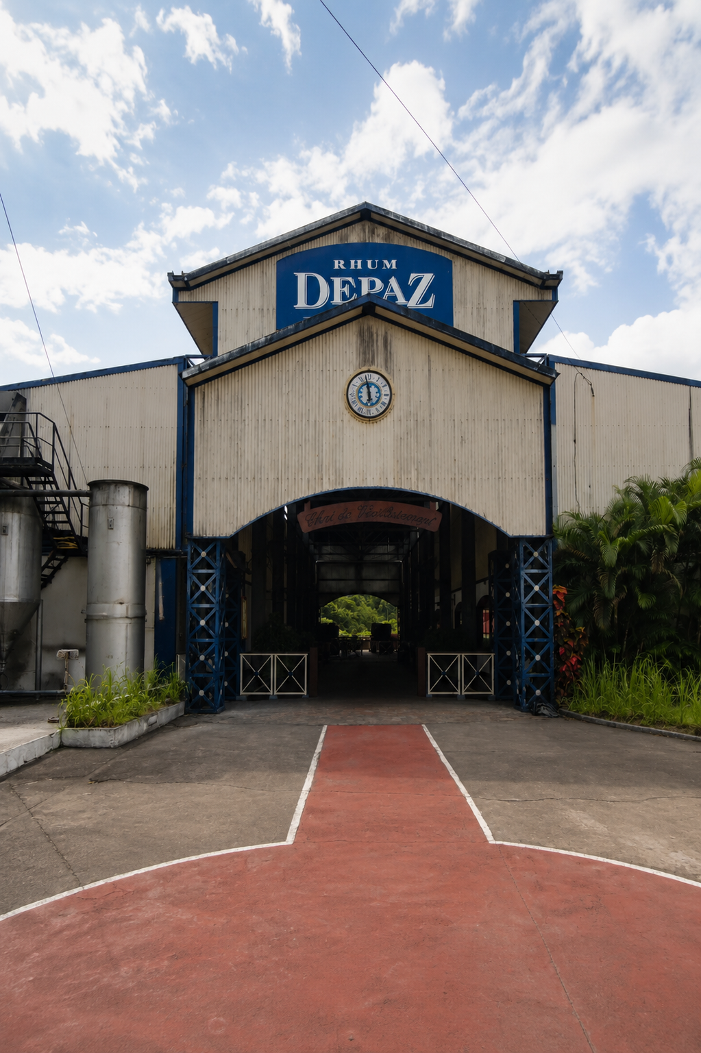 Entrée de la distillerie Depaz à Saint-Pierre : bâtiment industriel avec enseigne bleue au bout d'une allée bicolore.