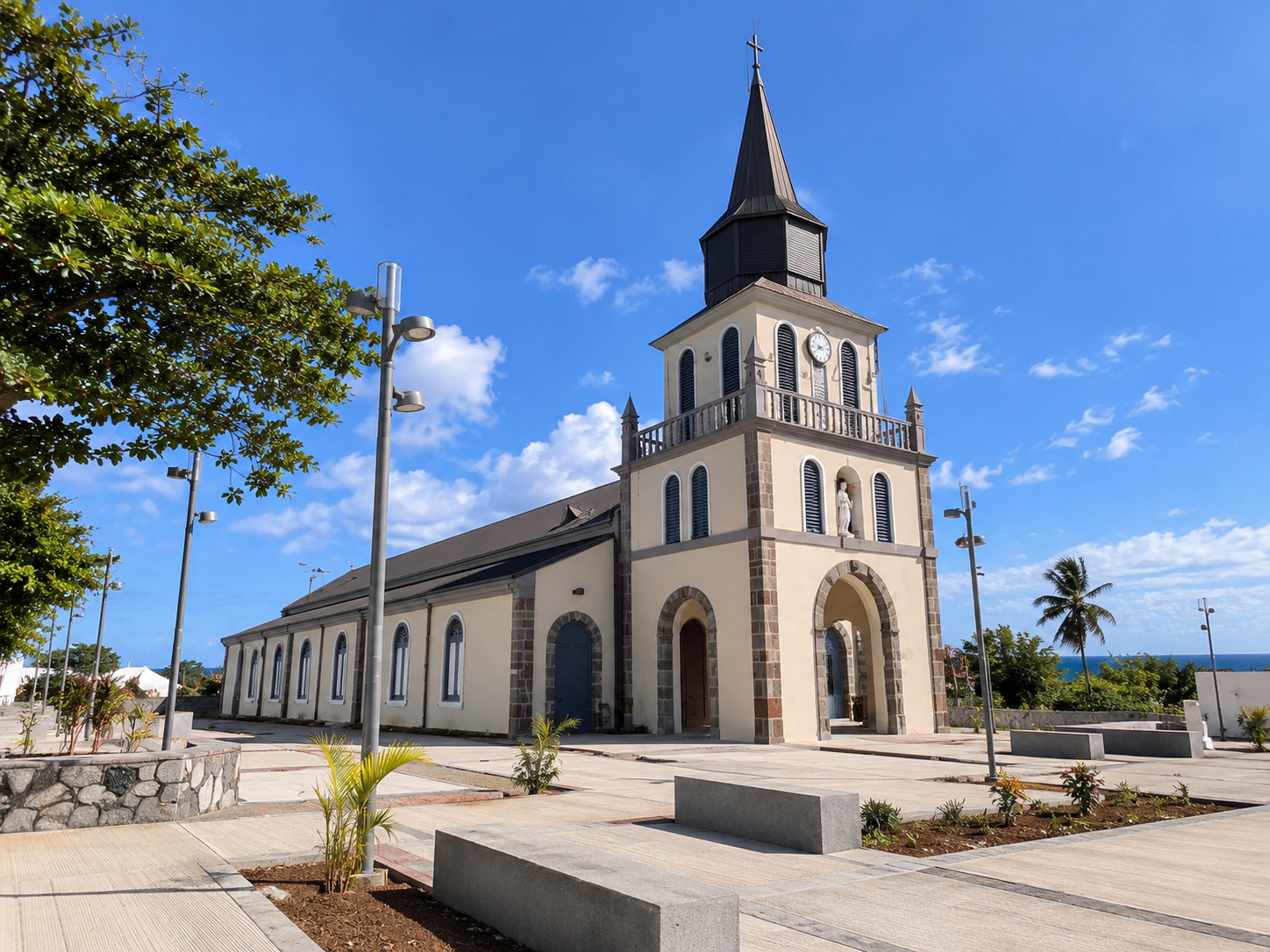 Église de Guadeloupe au bord de la mer, avec son clocher à flèche, sa façade en pierre et son parvis aménagé.