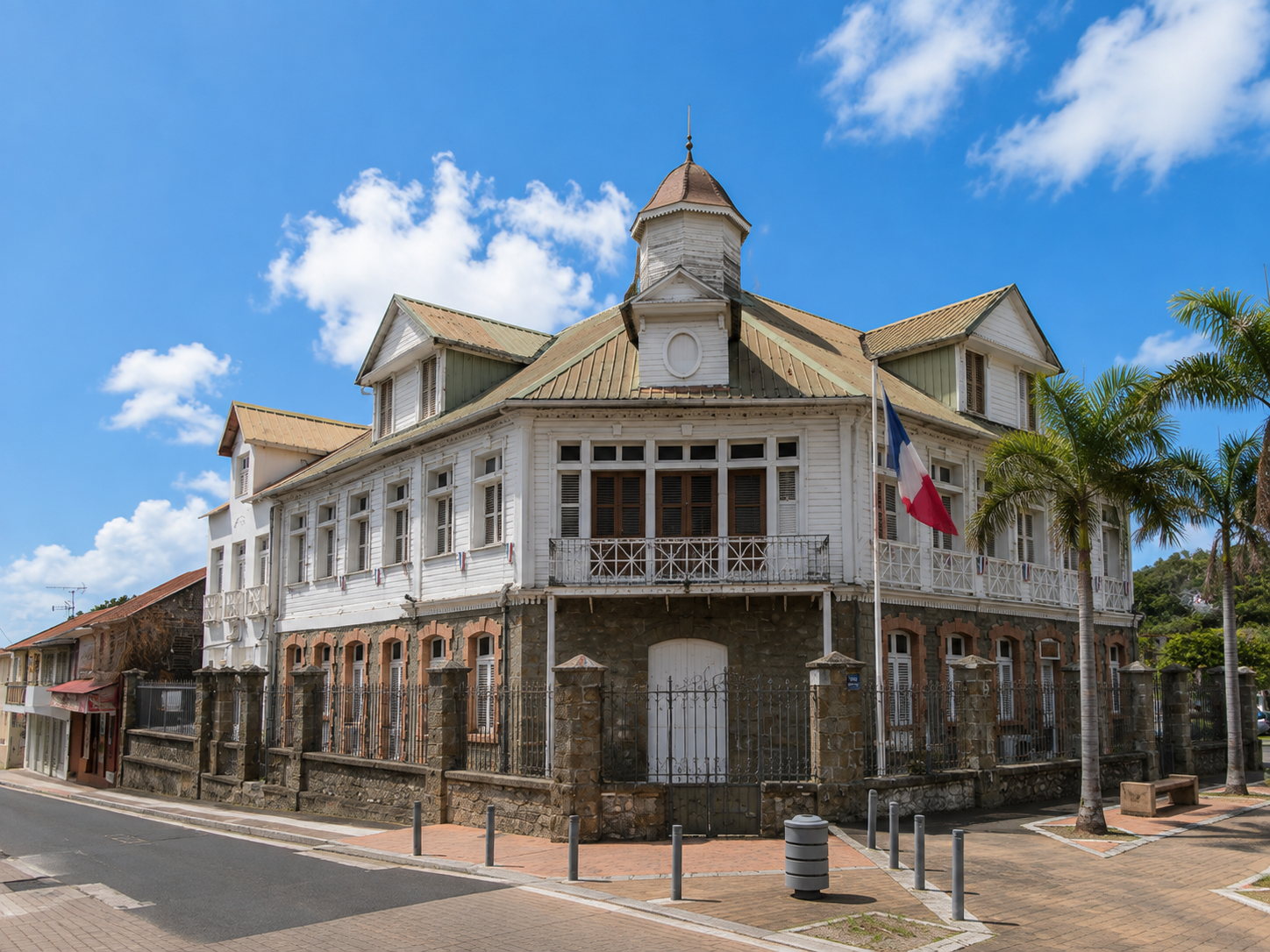 Façade en pierre et bois de l'hôtel de ville du François en Martinique avec le drapeau français sous le soleil.