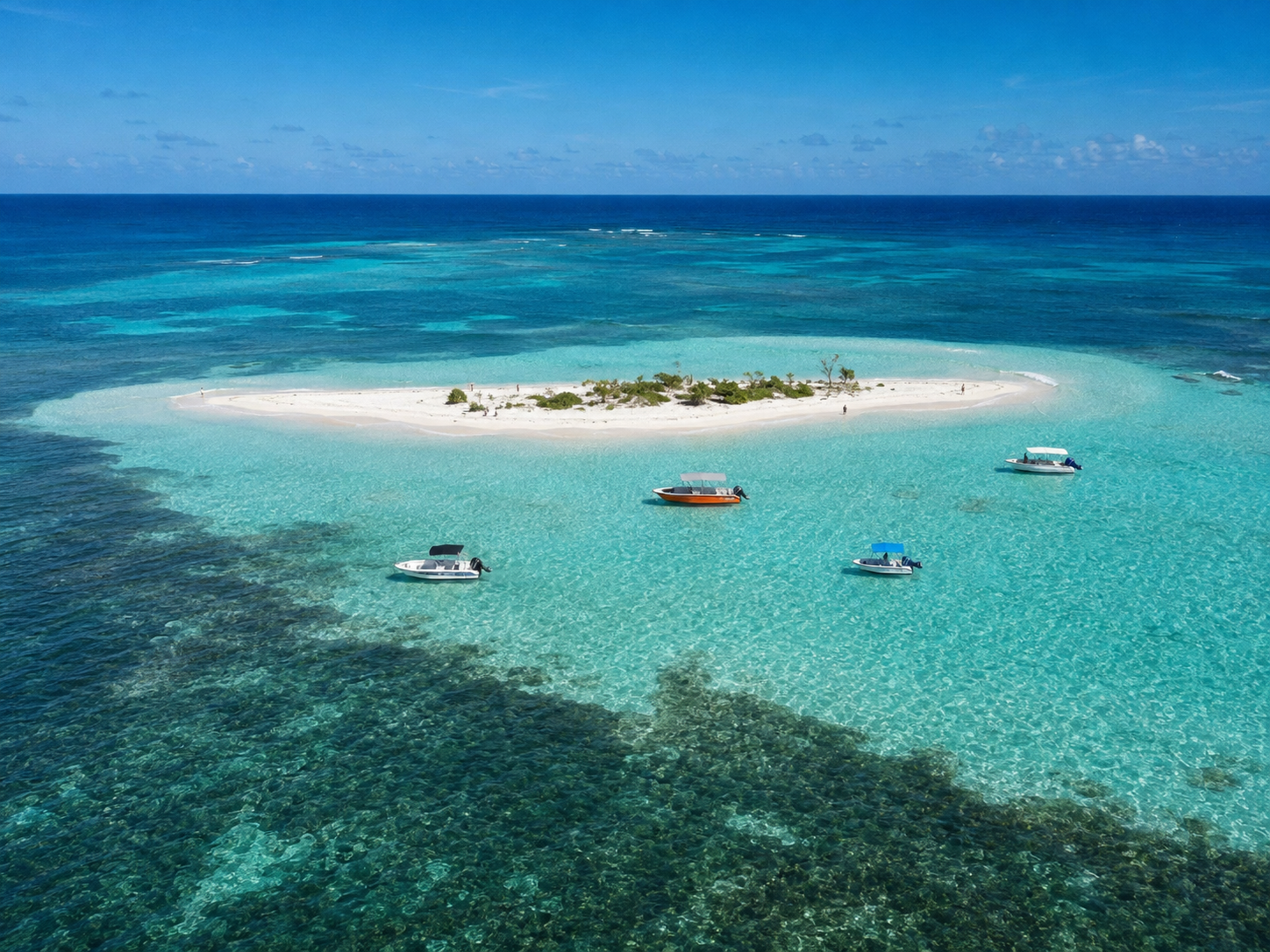Vue aérienne de l'îlet Caret et de ses fonds blancs dans le Grand Cul-de-Sac Marin en Guadeloupe, montrant une petite île de sable blanc entourée d'une eau turquoise translucide où mouillent plusieurs bateaux de plaisance.