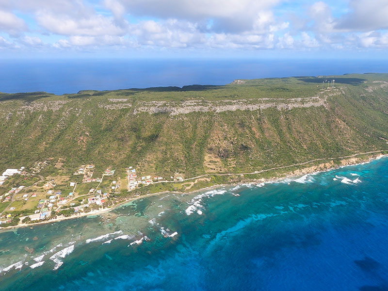 Vue aérienne de La Désirade en Guadeloupe : grand plateau rocheux verdoyant surplombant une mer bleu océan agitée.