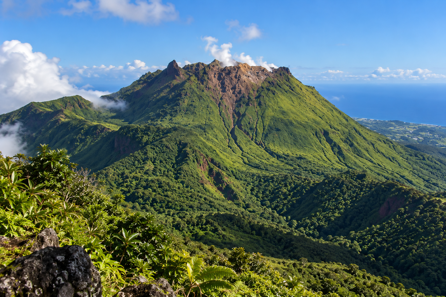 La Soufrière en Guadeloupe vue depuis les hauteurs, volcan verdoyant avec sommet rocheux, nuages et mer des Caraïbes.