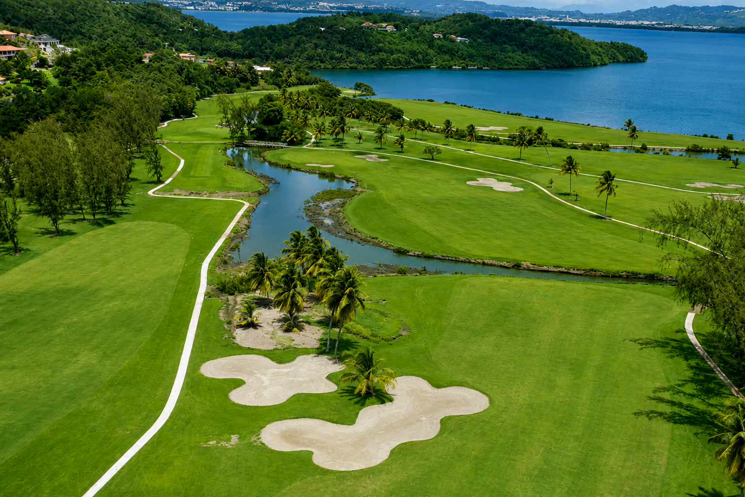 Golf de l'Espérance aux Trois-Îlets : parcours vert avec bunkers de sable, plan d'eau et vue sur la baie de Fort-de-France. 