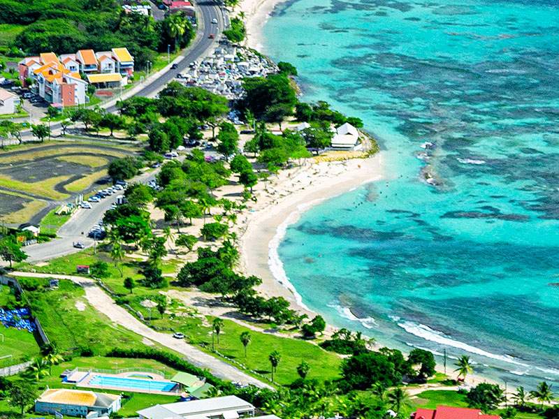 Vue aérienne de la plage des Raisins Clairs à Saint-François : sable blanc en croissant, lagon turquoise et arbres l'ombrant. 