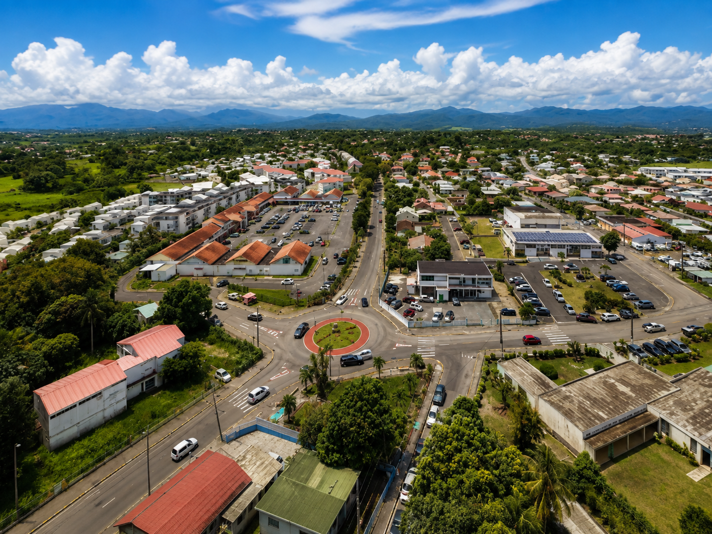 Vue aérienne du Lamentin en Martinique : rond-point fleuri au cœur de la ville, habitations et montagnes à l'horizon. (