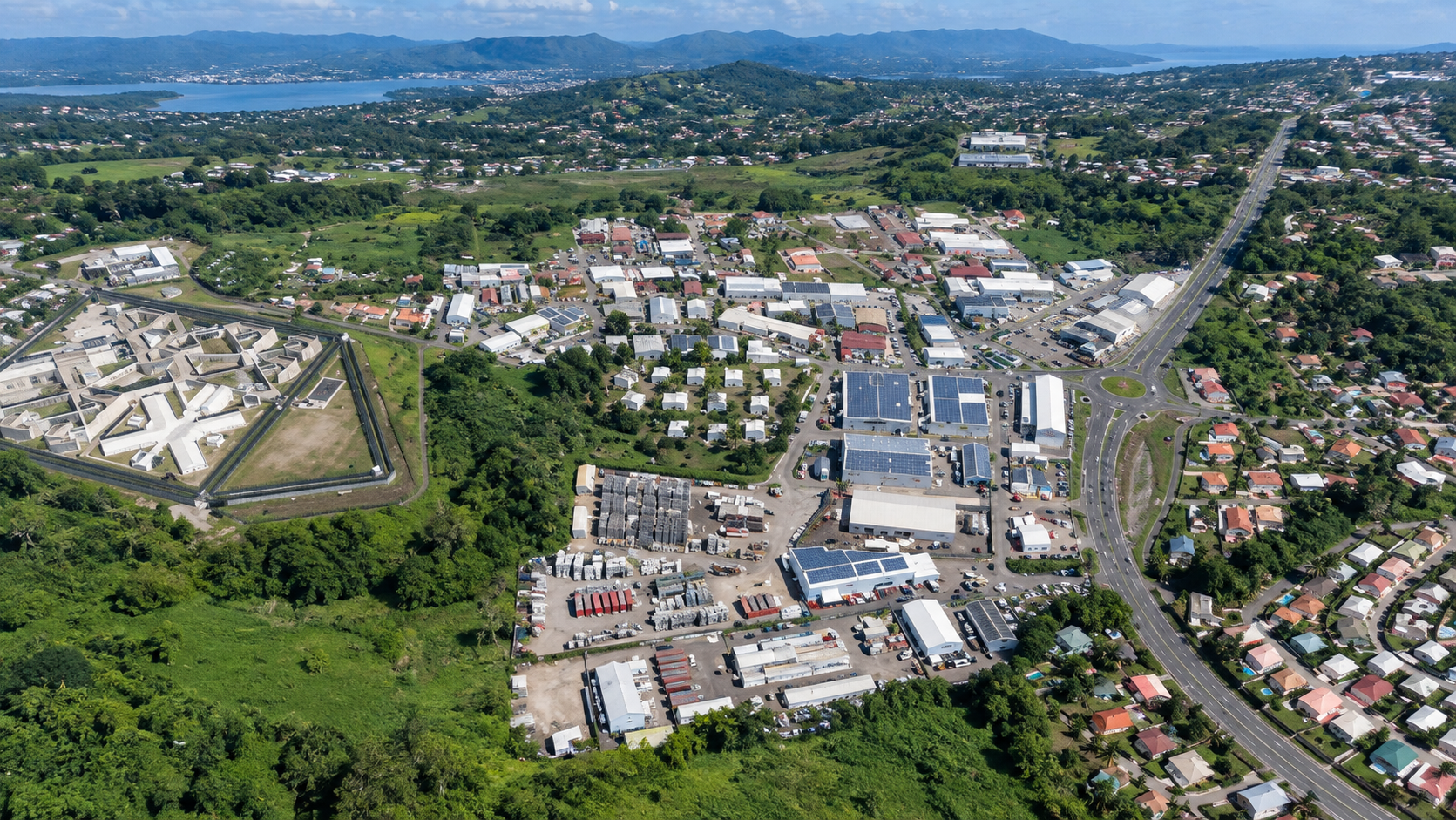 Vue aérienne hyper réaliste de la zone industrielle de Champigny à Ducos en Martinique, avec entrepôts, routes, entreprises et paysages verdoyants.