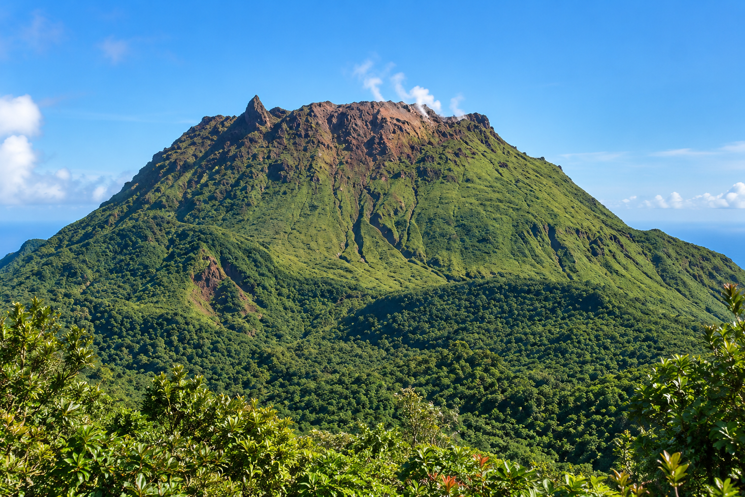 La Soufrière en Guadeloupe vue depuis les hauteurs, volcan verdoyant avec sommet rocheux, nuages et mer des Caraïbes.