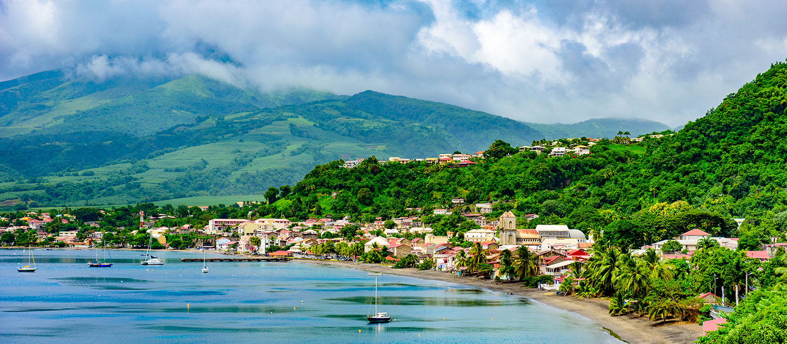 Ville côtière de Saint-Pierre en Martinique, installée au bord de l'eau au pied de montagnes verdoyantes sous les nuages. 