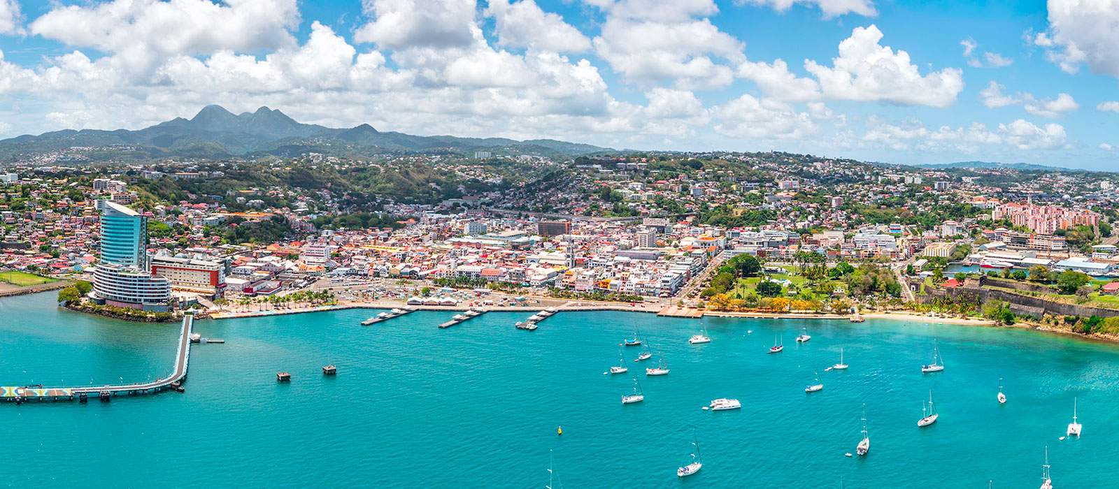 Vue aérienne de la baie de Fort-de-France en Martinique : mer turquoise parsemée de voiliers et tour Lumina en bord de mer. 