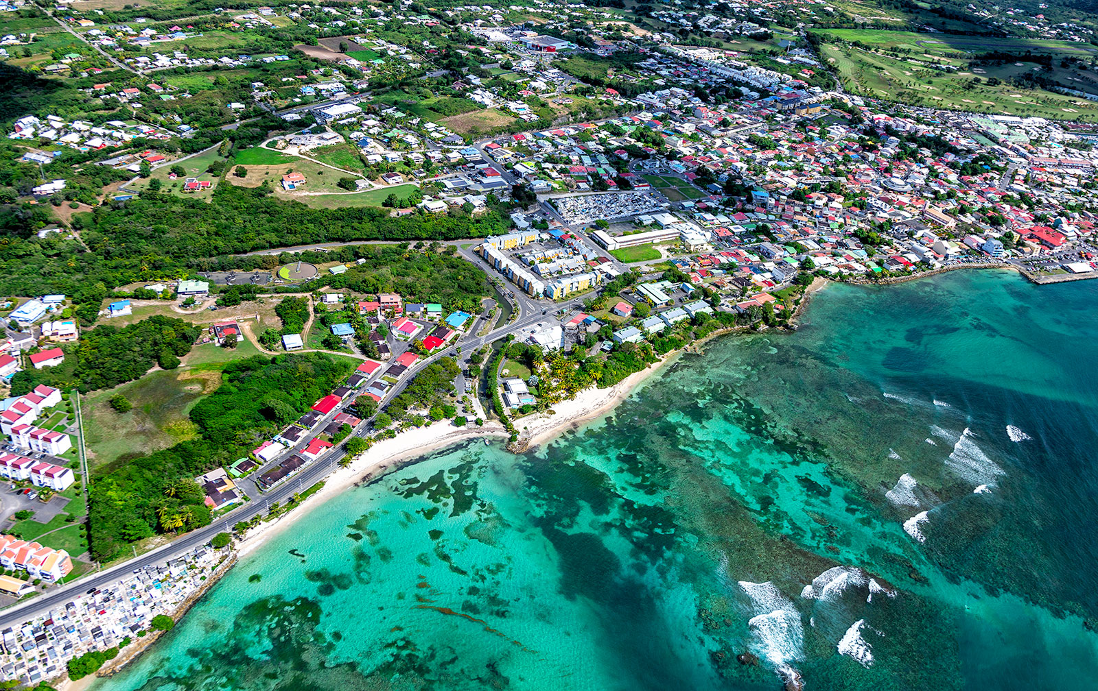 Vue aérienne de Saint-François en Guadeloupe : littoral rocheux, barrière de corail, eau turquoise et bourg urbain.