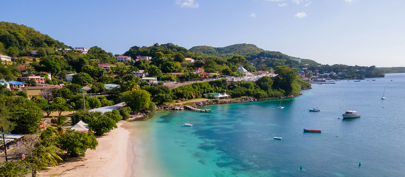 Vue panoramique de Sainte-Anne en Martinique : plage de sable blanc, mer turquoise transparente et bourg sur la colline. 